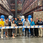 People standing in warehouse behind ribbon with Dot logos