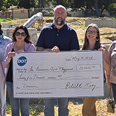 People holding large check for $25,000 outside at playground construction site